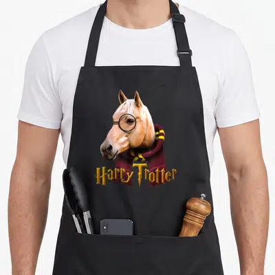 Tablier de cuisine noir avec tête de cheval Palomino portant des lunettes rondes et une écharpe maroon à rayures jaunes, sous le texte Harry Trotter doré.