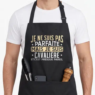 Tablier de cuisine noir avec inscription humoristique en lettres blanches et dorées sur fond uni.
