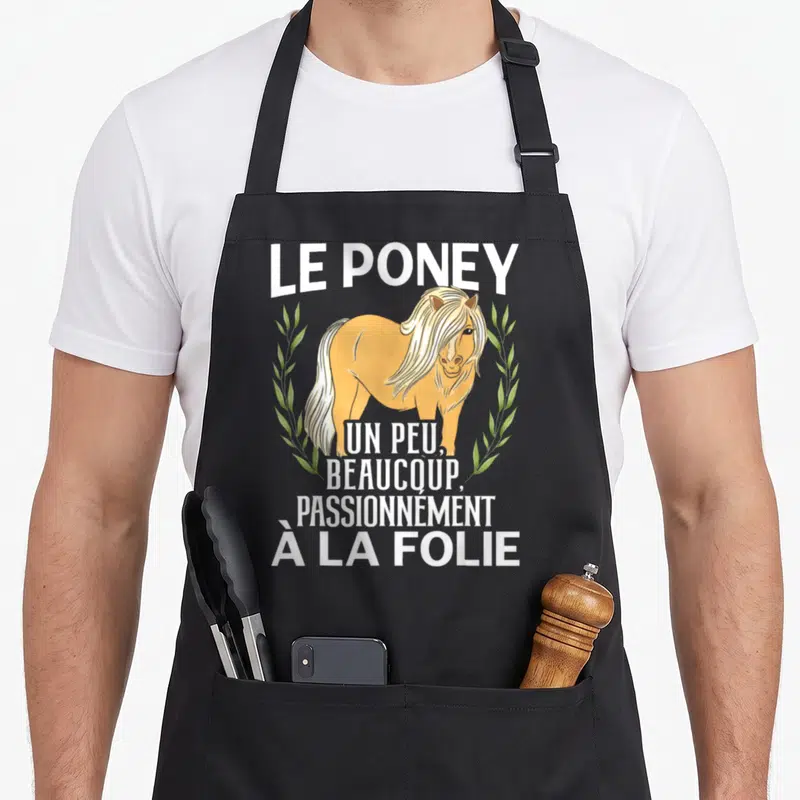 Tablier de cuisine noir avec illustration d'un poney blond et le texte Le poney un peu beaucoup passionnément à la folie entouré de feuillage vert.