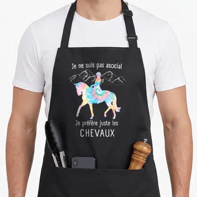 Tablier de cuisine noir avec un cheval aux couleurs tie-dye et une silhouette de cavalière sur fond de montagnes.