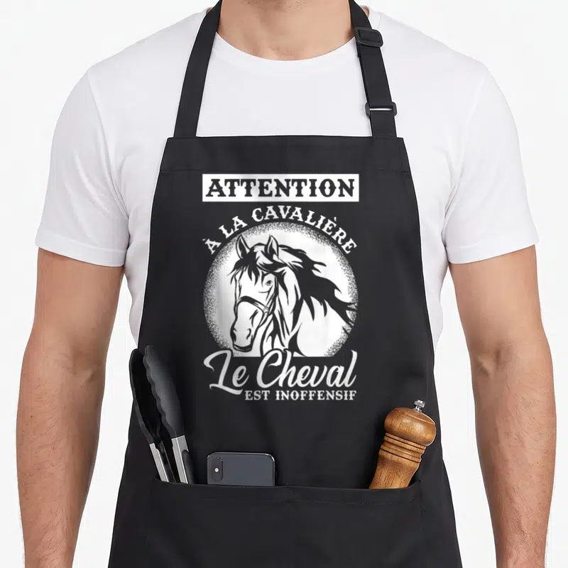 Tablier de cuisine noir avec illustration blanche d'une tête de cheval et le texte attention à la cavalière le cheval est inoffensif.