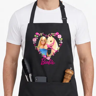 Tablier de cuisine noir avec Barbie et un cheval blond dans un cœur de fleurs roses et le logo Barbie en bas.