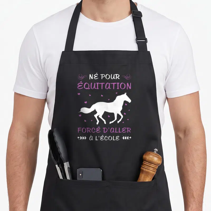 Tablier de cuisine noir avec silhouette de cheval blanc et texte humoristique sur l'équitation et l'école en lettres roses et blanches.