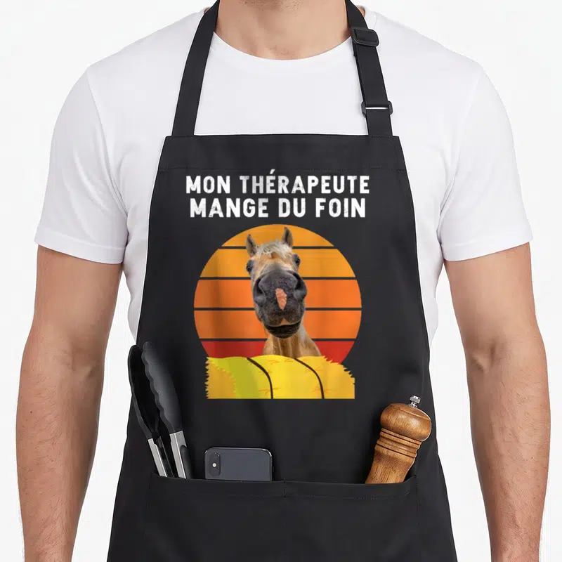 Tablier de cuisine noir avec inscription mon thérapeute mange du foin et portrait de cheval sur fond orange rayé.
