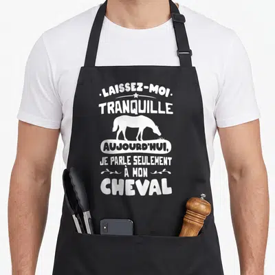 Tablier de cuisine noir avec inscription blanche Laissez-moi tranquille et silhouette de cheval broutant l'herbe au centre du vêtement.