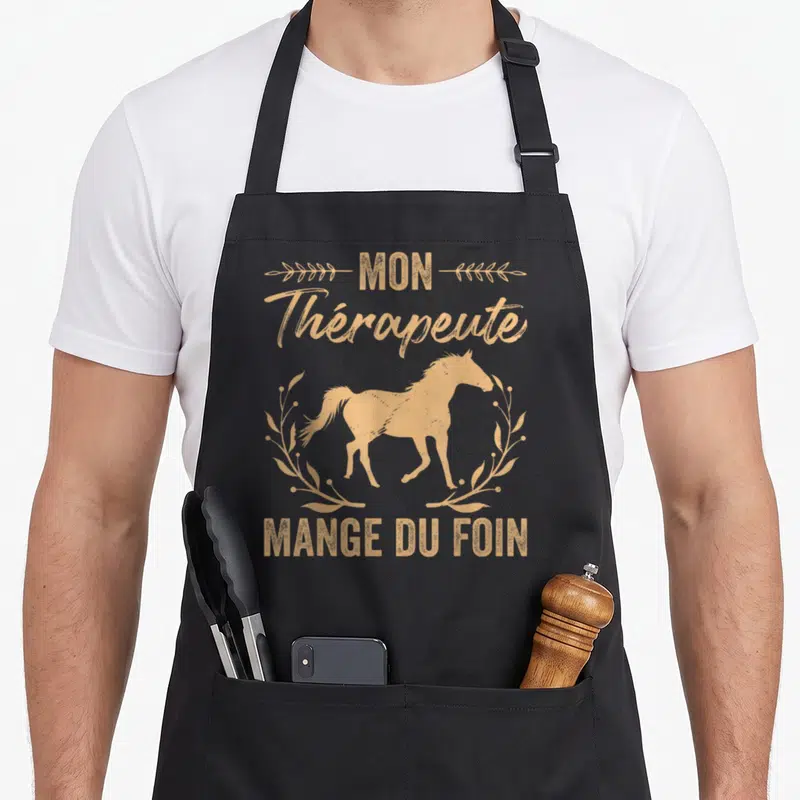 Tablier de cuisine noir avec silhouette de cheval dorée et texte Mon thérapeute mange du foin encadré de branches stylisées.