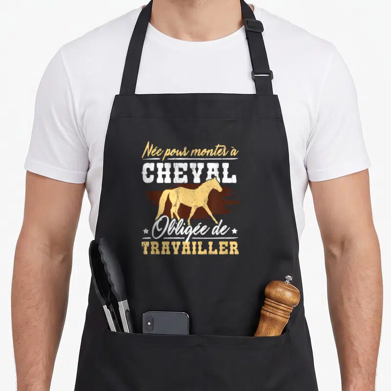 Tablier de cuisine noir avec silhouette de cheval doré et texte blanc et jaune Née pour monter à cheval obligée de travailler.
