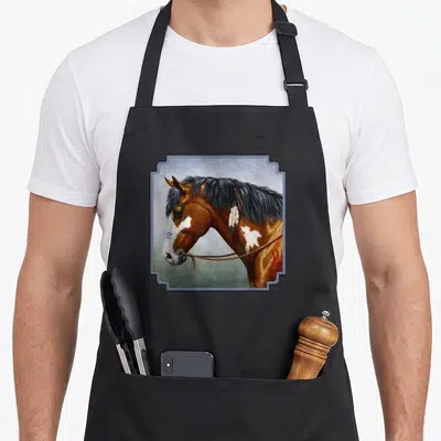 Tablier de cuisine noir avec portrait de cheval Bay Pinto orné d'une plume et de peintures tribales dans un cadre décoratif.