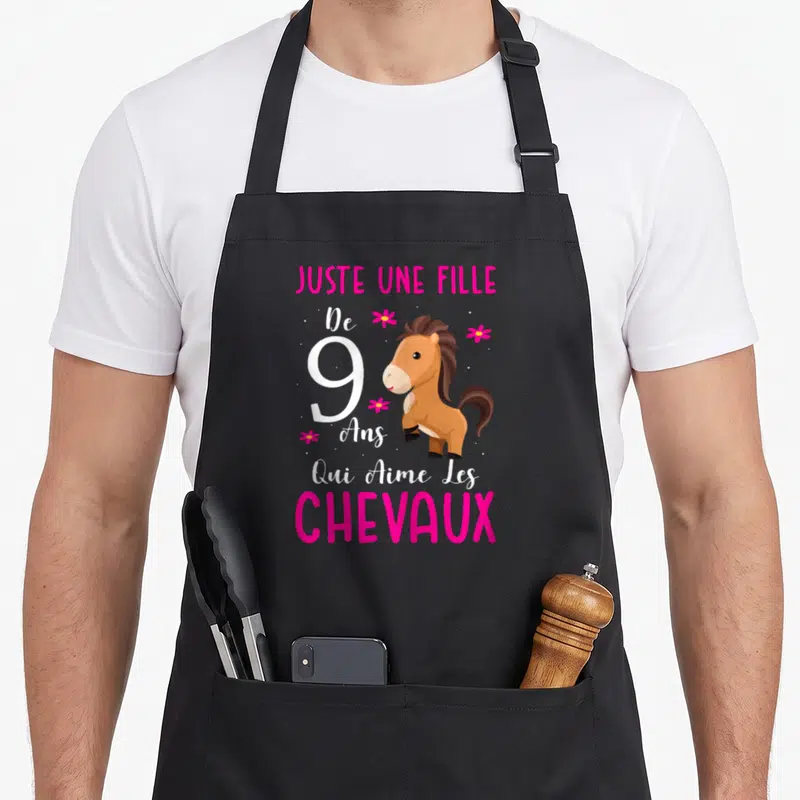 Tablier de cuisine noir avec illustration d'un poney marron et texte rose indiquant l'âge et le goût pour les équidés.