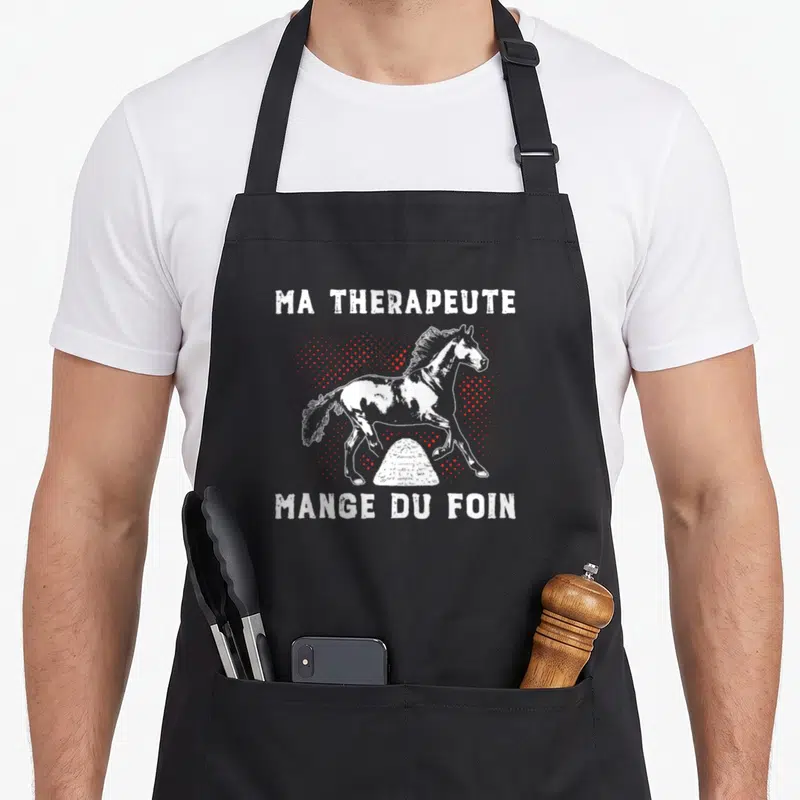 Tablier de cuisine noir avec illustration d'un poney blanc et le texte Ma thérapeute mange du foin en lettres capitales blanches.