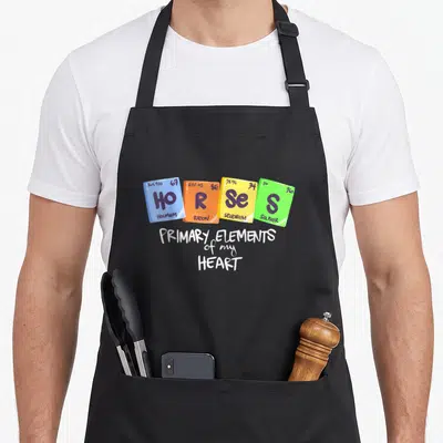 Tablier de cuisine noir avec quatre cases colorées du tableau périodique et un texte blanc sous-jacent.