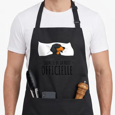 Tablier de cuisine noir avec illustration d'un teckel au lit et texte « Chemise de la nuit officielle ».