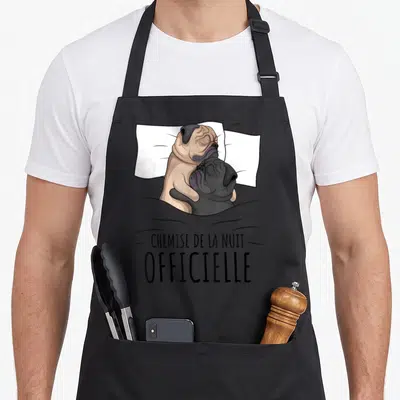 Tablier de cuisine noir avec deux carlins enlacés sous une couverture et le texte « chemise de la nuit ».