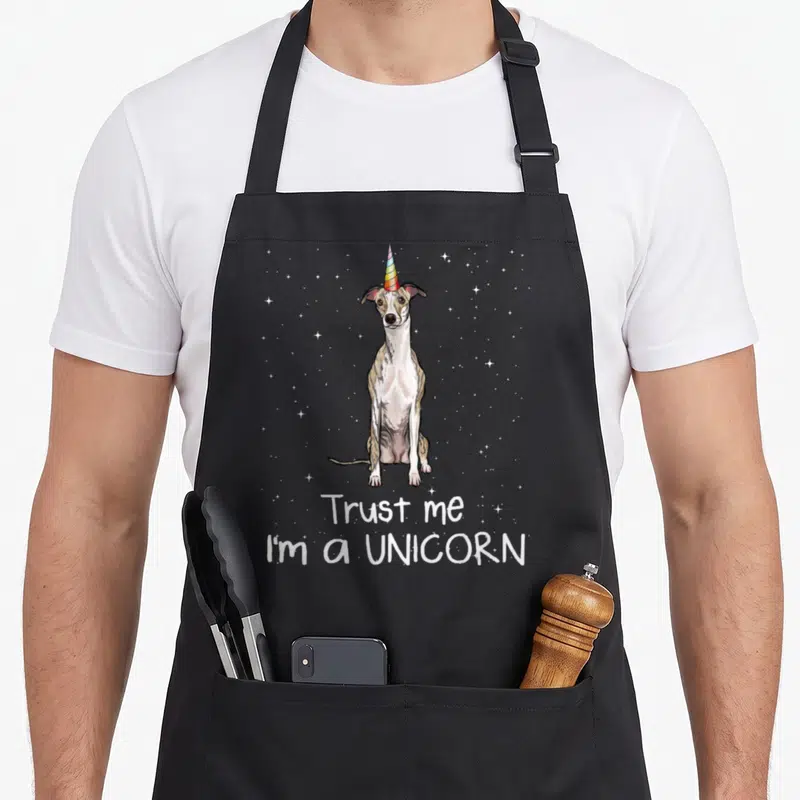 Tablier de cuisine noir avec illustration d'un whippet portant une corne multicolore et des étoiles en arrière-plan.