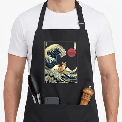 Tablier de cuisine noir avec illustration d'un Corgi fawn surfant sur une grande onde bleue style gravure japonaise et un soleil rouge en arrière-plan.