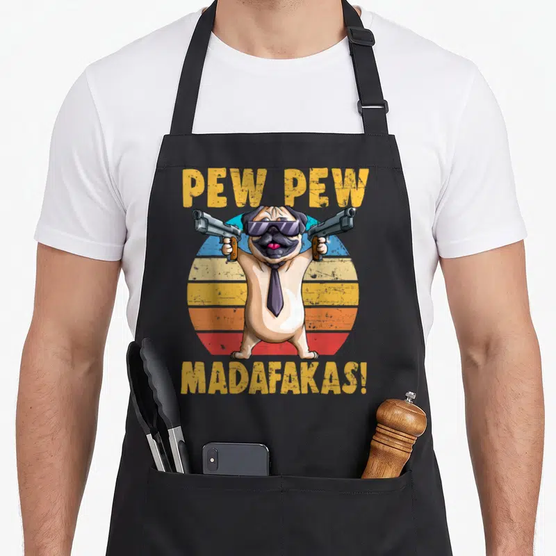 Tablier de cuisine noir avec illustration d'un pug portant des lunettes noires et tenant deux revolvers devant un fond coloré.