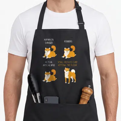 Tablier de cuisine noir avec illustrations de Shiba Inu et textes anglais humoristiques sur les risques humains et les chipettes.