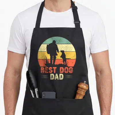 Tablier de cuisine noir avec silhouette homme et chien devant un soleil rayé multicolore et le texte Best Dog Dad.