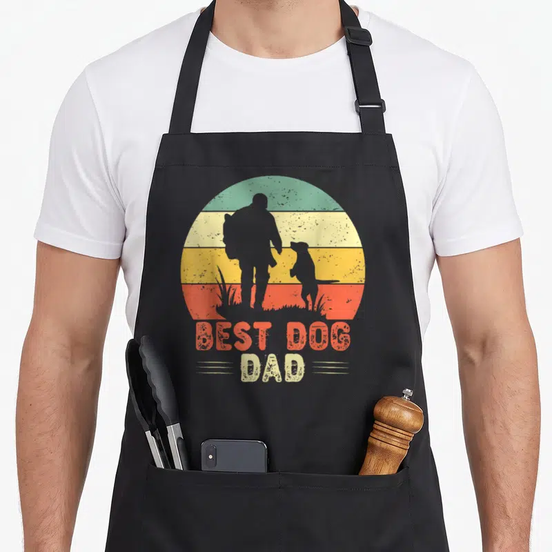 Tablier de cuisine noir avec silhouette homme et chien devant un soleil rayé multicolore et le texte Best Dog Dad.