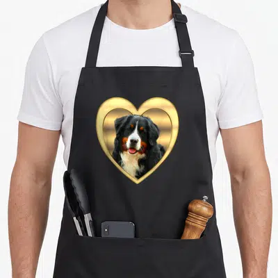 Tablier de cuisine noir avec un Bouvier bernois souriant encadré par un cœur doré brillant.
