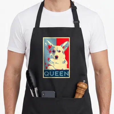 Tablier de cuisine noir avec illustration pop art d'un corgi blanc et rouge sur fond bleu et rouge, texte QUEEN en bas.