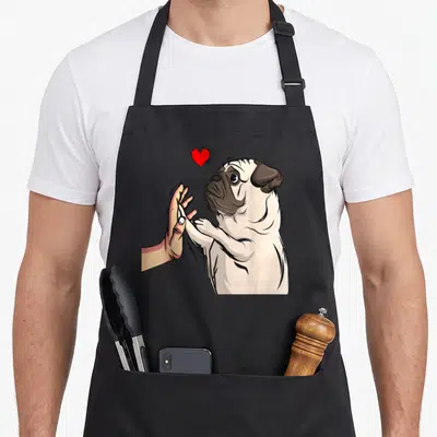 Tablier de cuisine noir avec illustration d'un pug tenant une main humaine sous un cœur rouge.