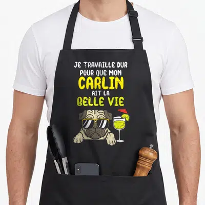 Tablier de cuisine noir avec un carlin en lunettes de soleil, un cocktail et le texte Je travaille dur pour que mon carlin ait la belle vie.