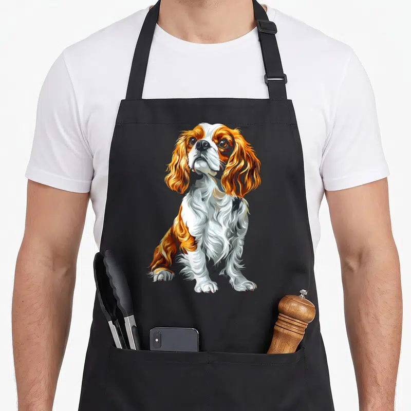 Tablier de cuisine noir avec illustration colorée d'un chien Cavalier King Charles Spaniel assis regardant vers le haut