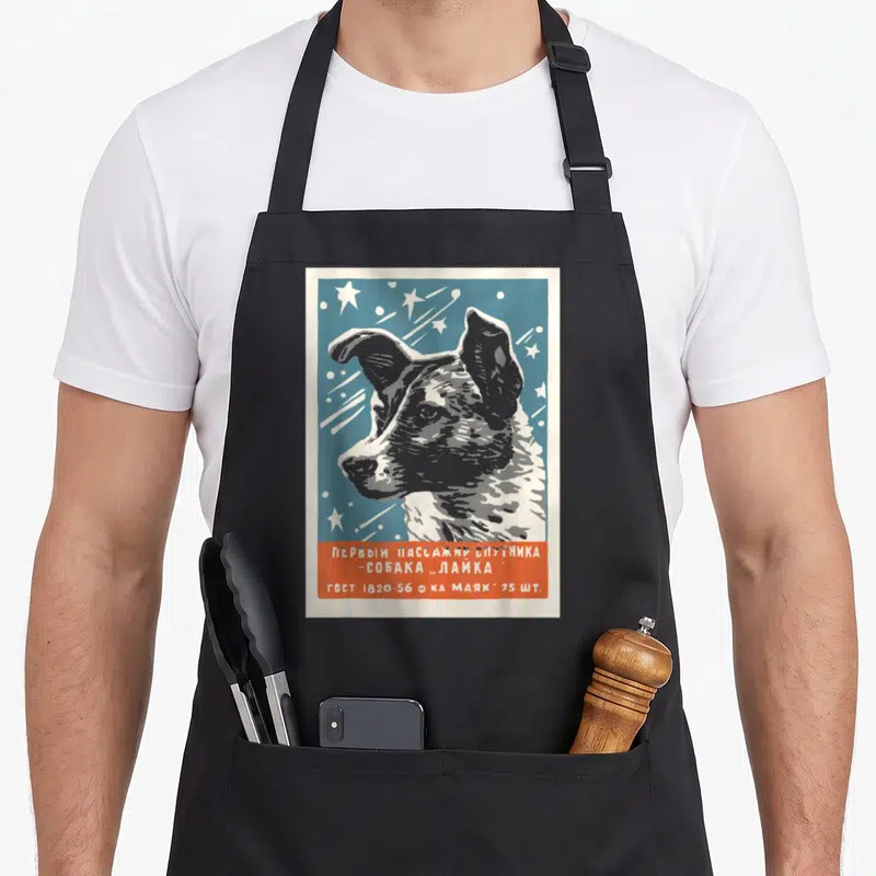 Tablier de cuisine noir avec illustration vintage de Laika et texte en alphabet cyrillique sur fond bleu et orange.