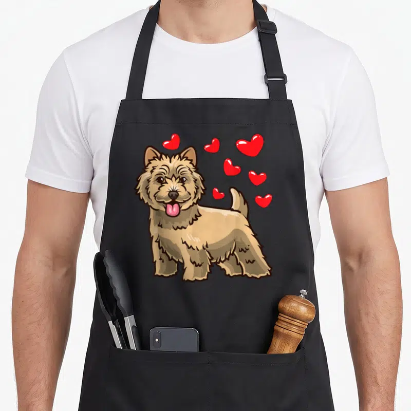Tablier de cuisine noir avec un Cairn Terrier marron et des cœurs rouges flottants autour de sa tête.