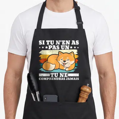 Tablier de cuisine noir avec un Shiba Inu orange dormant et une phrase humoristique en blanc sur bandes colorées.