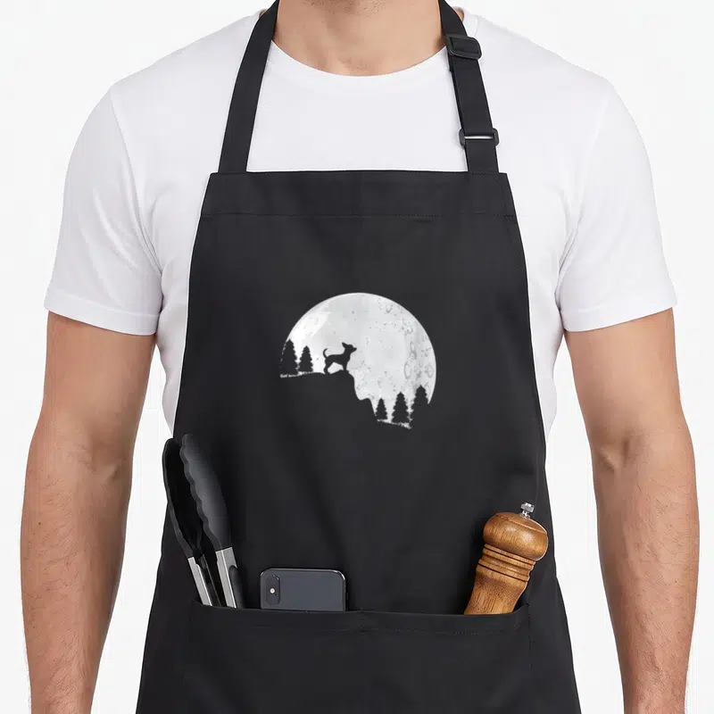 Tablier de cuisine noir avec silhouette de petit chien sur un rocher face à une grande lune pleine.