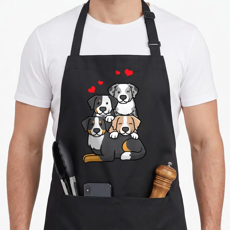Tablier de cuisine noir avec quatre chiens dessinés en cartoon et des cœurs rouges flottant au-dessus.