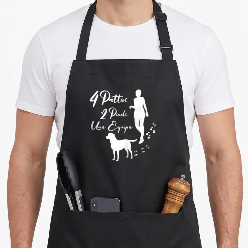 Tablier de cuisine noir avec silhouette humaine et chien blanc, texte 4 Pattes 2 Pieds Une Équipe et traces de pas.