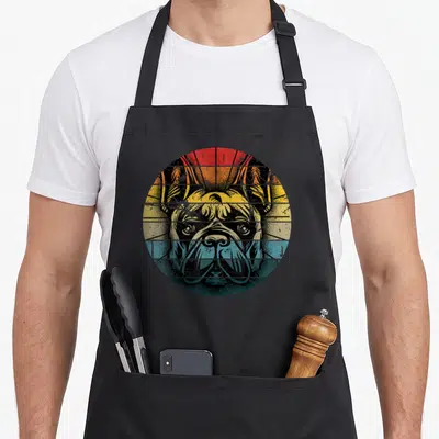 Tablier de cuisine noir avec illustration circulaire d'un bouledogue français aux couleurs orange et bleu sur fond rayé.