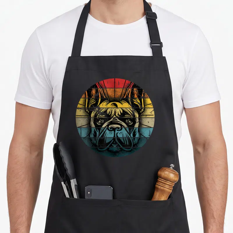Tablier de cuisine noir avec illustration circulaire d'un bouledogue français aux couleurs orange et bleu sur fond rayé.