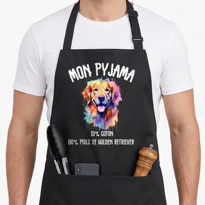 Tablier de cuisine noir avec tête de Golden Retriever multicolore et texte blanc humoristique sur fond uni.
