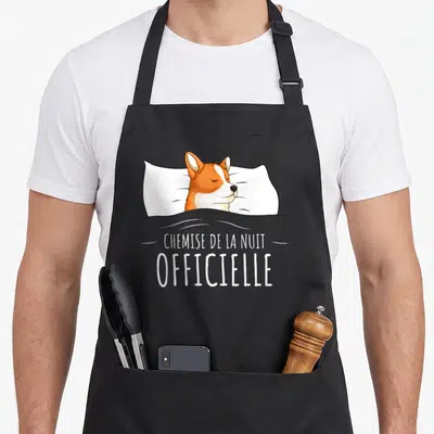 Tablier de cuisine noir avec illustration d'un corgi dormant sur un oreiller blanc et le texte "chemise de la nuit" imprimé en blanc.