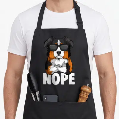 Tablier de cuisine noir avec un chien berger australien en lunettes noires et le texte NOPE imprimé en blanc.