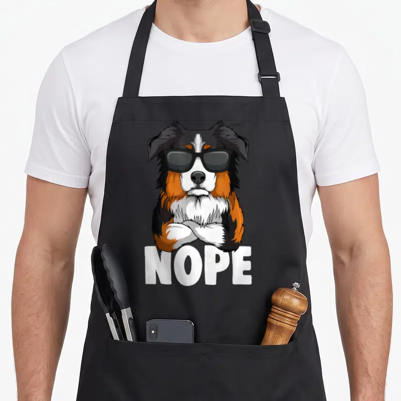 Tablier de cuisine noir avec un chien berger australien en lunettes noires et le texte NOPE imprimé en blanc.