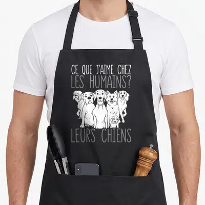 Tablier de cuisine noir avec une illustration blanche de cinq chiens et le texte Ce que j'aime chez les humains leurs chiens.
