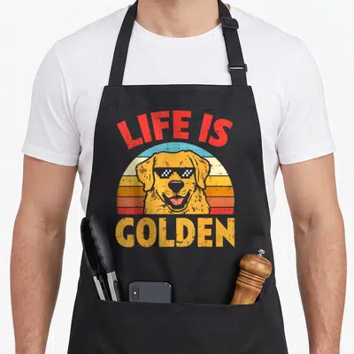 Tablier de cuisine noir avec illustration d'un golden retriever aux lunettes de soleil pixelisées et texte Life Is Golden en lettres colorées.