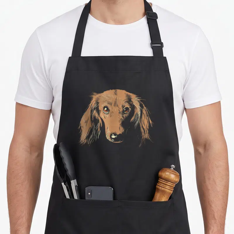 Tablier de cuisine noir avec illustration stylisée d'un teckel wiener au regard doux et aux poils longs détaillés.
