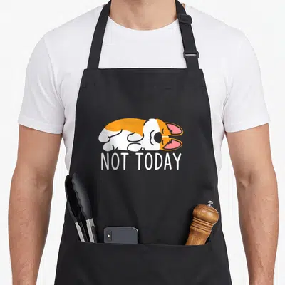 Tablier de cuisine noir avec illustration d'un corgi orange et blanc dormant et le texte NOT TODAY en lettres capitales blanches.