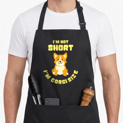 Tablier de cuisine noir avec un corgi assis et le texte jaune I'm Not Short I'm Corgi Size.