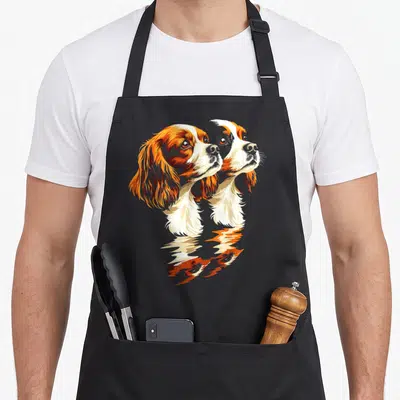 Tablier de cuisine noir avec illustration de deux têtes de chien Cavalier King Charles Spaniel et leur reflet stylisé.