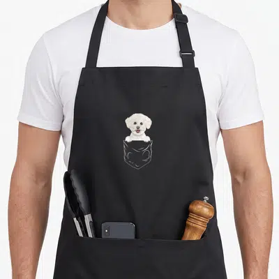 Tablier de cuisine noir avec un Bichon Frise blanc souriant sortant d'une poche dessinée en contour.