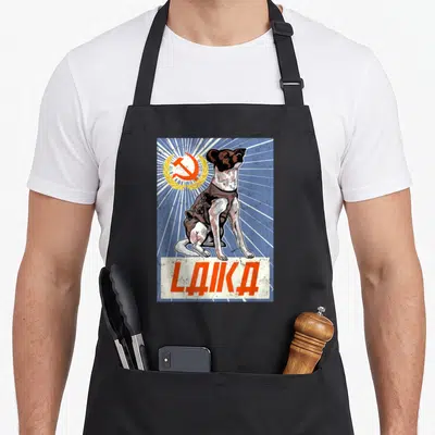 Tablier de cuisine noir avec illustration de Laika chien spatial et texte LIKA en style propagande soviétique.