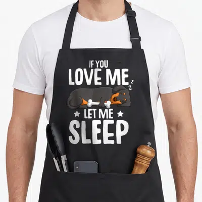Tablier de cuisine noir avec un teckel endormi tenant une os et le texte If You Love Me Let Me Sleep en blanc.