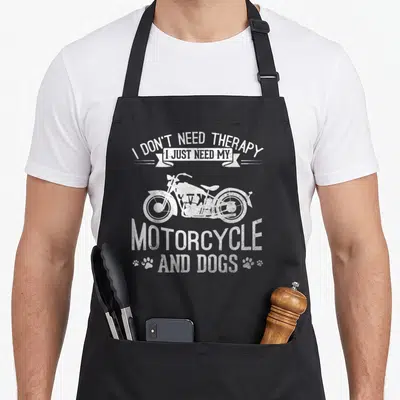 Tablier de cuisine noir avec illustration de moto vintage, traces de pattes et texte humoristique en blanc.
